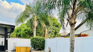 Un patio trasero bien cuidado con césped, una palmera y un jacuzzi de madera.
