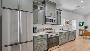 A modern kitchen with stainless steel appliances, grey cabinets, and wooden flooring. - Tiny Twin Mia, Charming 2-bedroom house in wonderful Waco- fully furnished (Waco)