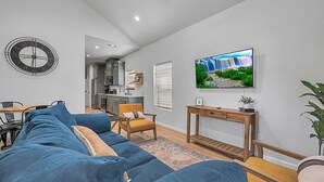 A modern living room with a blue sectional sofa, a wooden coffee table, and a TV mounted on the wall. - Tiny Twin Mia, Charming 2-bedroom house in wonderful Waco- fully furnished (Waco)