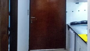 A narrow hallway with a wooden door at the end, leading to a kitchen area with white cabinets and a yellow countertop. - Porteño Heart Santa Fe and Cerrito (Buenos Aires)