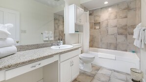 Une salle de bain moderne avec un lavabo sur un plan de travail en granit, des meubles blancs, des toilettes et une baignoire.