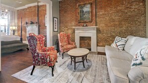 A living room with a brick wall, a fireplace, a sofa, and two patterned armchairs.