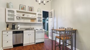 A compact kitchen with white cabinetry, a dishwasher, an oven, and a dining table with two chairs.