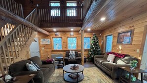 Interior acogedor de una cabaña con paredes de madera, una escalera, un árbol de Navidad y dos sofás.