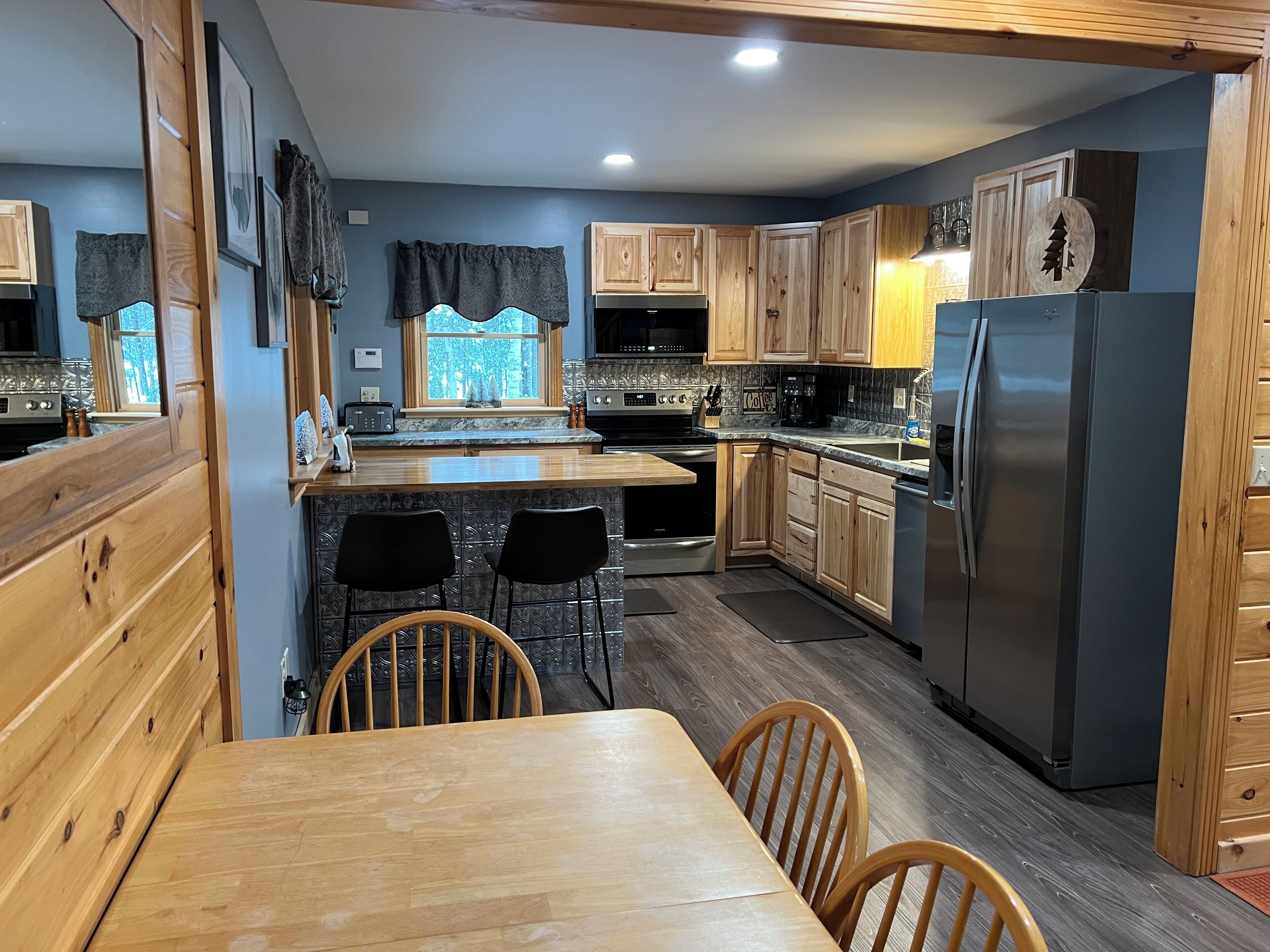 A kitchen with wooden cabinets, a stainless steel refrigerator, a built-in oven, and a window with a view.
