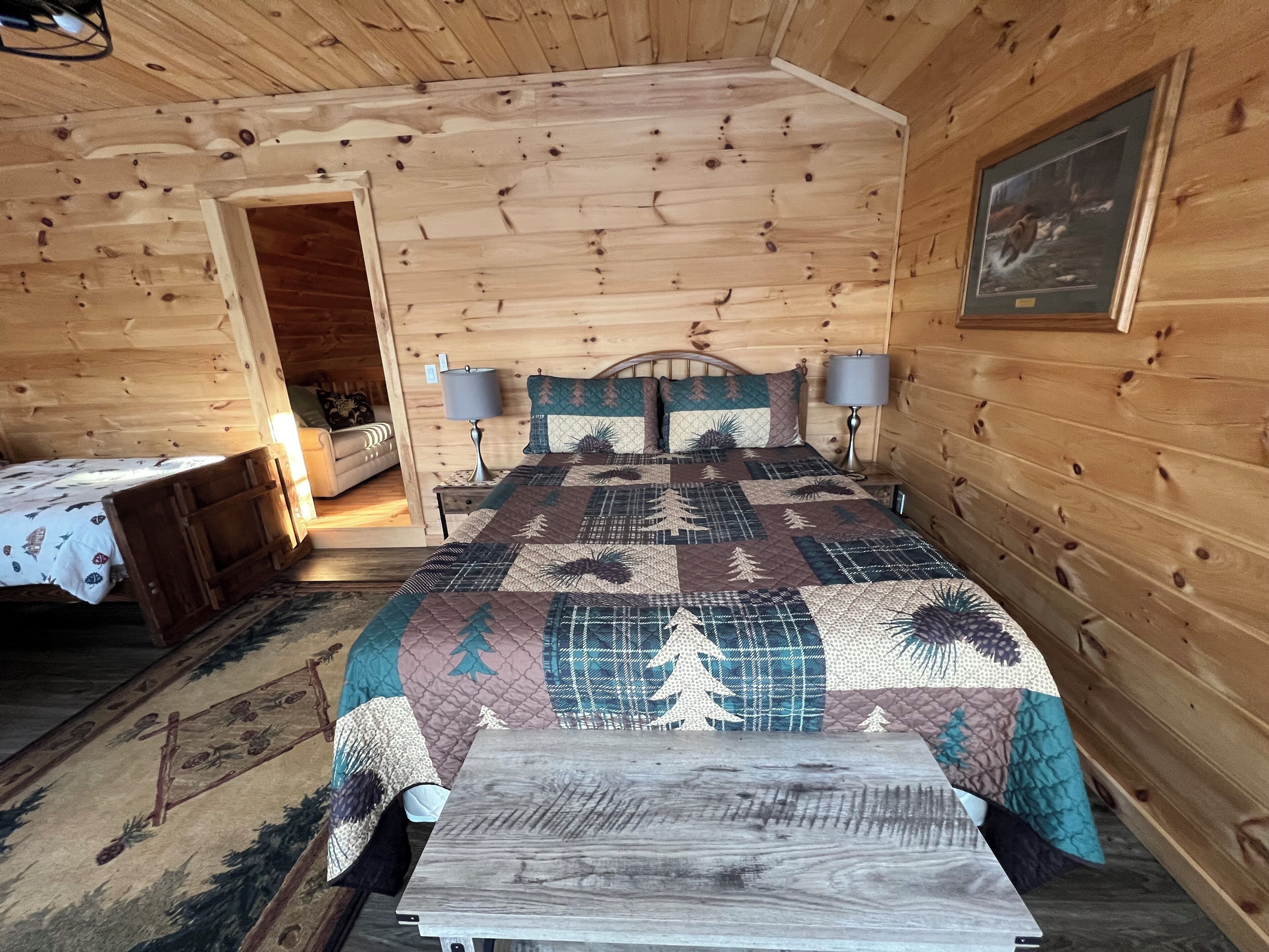 A wooden cabin bedroom with a bed, two bedside tables, a nightstand, and a painting on the wall.