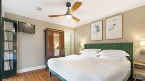 Habitación de hotel con una cama grande, ventilador de techo, televisión, armario de madera y cuadros en las paredes.