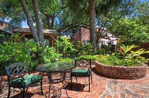 Un patio con una mesa de vidrio, dos sillas y una jardinera de ladrillo.