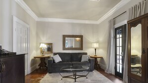Un salón con un sofá de color oscuro, una mesa de centro de vidrio, un mueble de madera, un espejo y una puerta con cortinas.