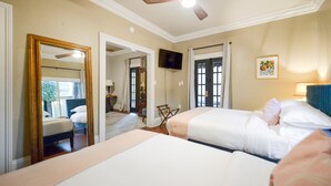 Habitación de hotel con dos camas, ventilador de techo, televisión y un espejo grande.