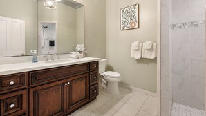 A bathroom with a wooden vanity, a large mirror, a shower, and a toilet.
