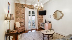 Una sala de estar con pared de ladrillo, una araña, televisor, sofá, mesa de centro y puerta que da al exterior.