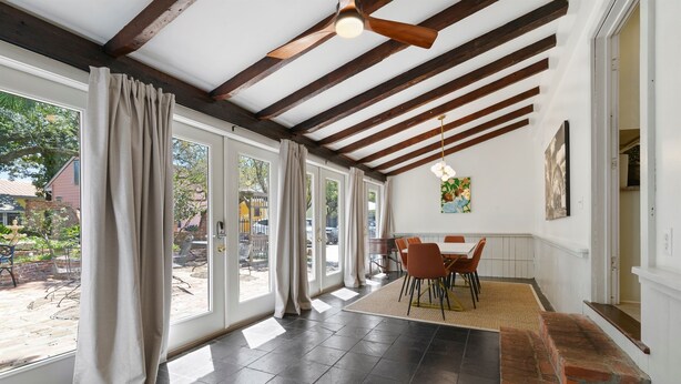 Amplia habitación con techo alto, vigas de madera a la vista, chimenea de ladrillo y grandes ventanales con cortinas.