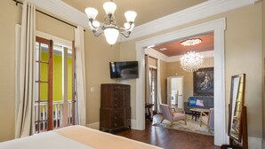 A hotel room with a large bed, a dresser, a television, a chandelier, and a painting on the wall.