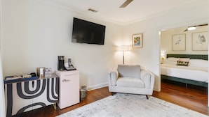 Une chambre à coucher comprenant un lit, un bureau avec une machine à café, une chaise, une télévision et des œuvres d’art accrochées au mur.
