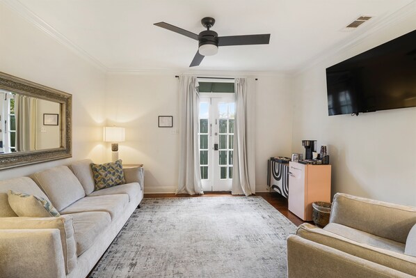 Un salon comprenant un canapé, une table basse, un téléviseur, un ventilateur de plafond et une porte donnant sur l’extérieur.