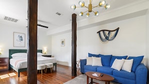 A room with a bed, a blue sofa, a wooden coffee table, and a chandelier. - The Shorty Guest House (New Orleans)