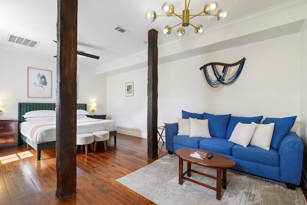 A room with a bed, a blue sofa, a wooden coffee table, and a chandelier. - The Shorty Guest House (New Orleans)