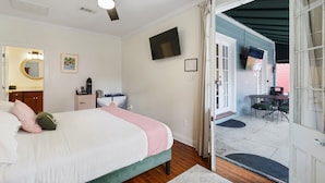 Un dormitorio con cama, ventilador de techo, televisor y vistas al patio exterior.