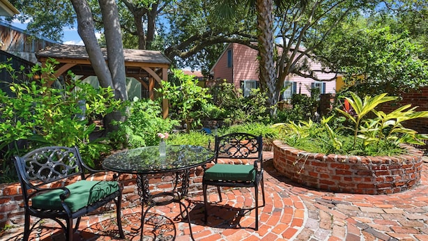 Un patio con una mesa de vidrio, dos sillas y una jardinera de ladrillo.