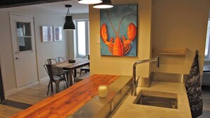 Een moderne keuken met een houten aanrecht, een roestvrijstalen spoelbak en een schilderij van een kreeft aan de muur.