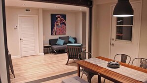 Een eetgedeelte met een houten tafel, stoelen en een hanglamp. Achtergrond is een bank met kussens.
