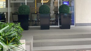 Entrada de hotel con puertas de vidrio, plantas en macetas y un letrero visible de SMDC.