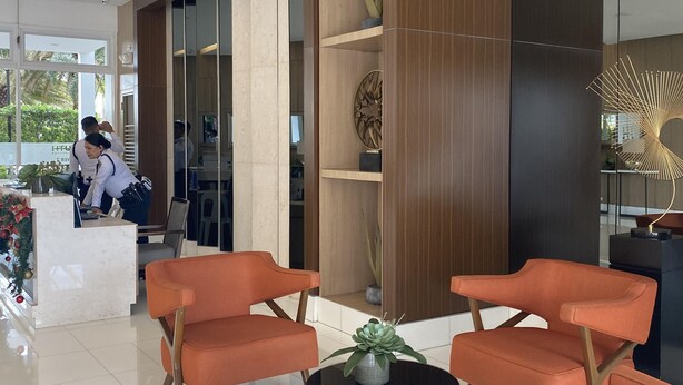 Una zona de recepción moderna con mostrador de mármol, sillas color naranja y una planta decorativa.