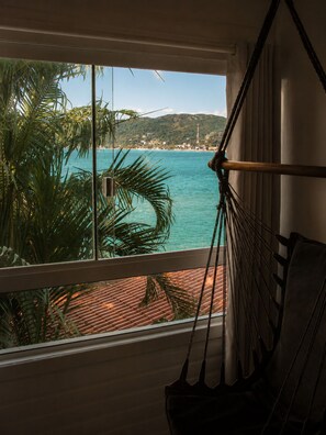 A room with a view of a beach and ocean, a hammock, and a window with blinds. - Lagoa Nômade (Florianópolis)