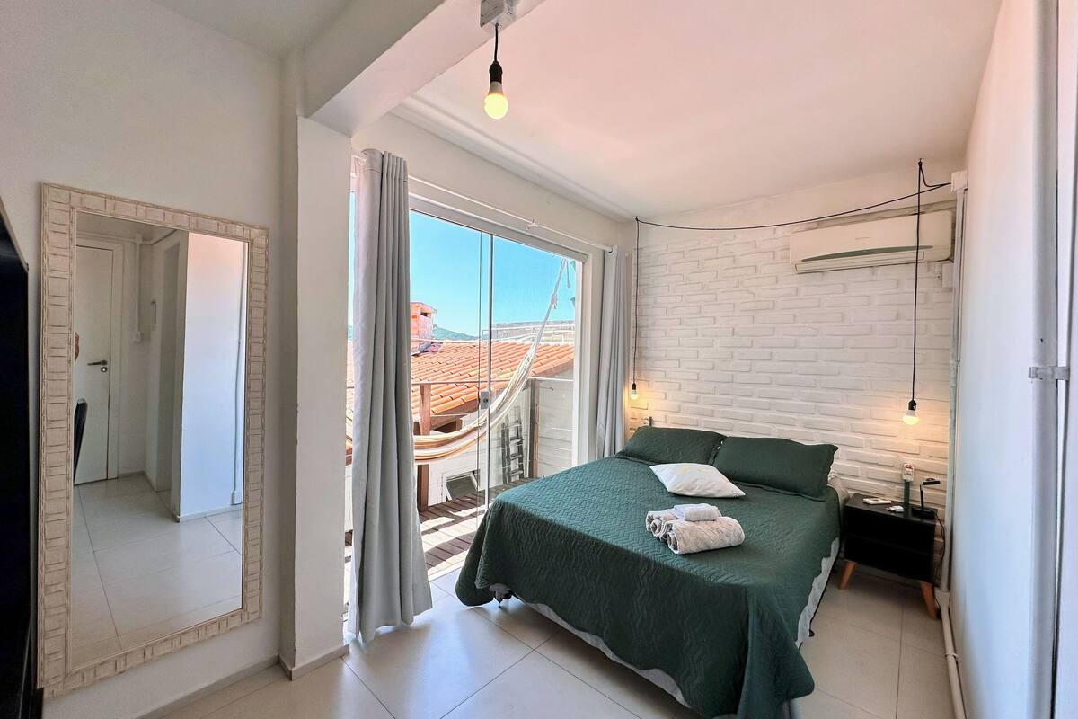 A bedroom with a bed, a nightstand, a mirror, and a window with curtains.
