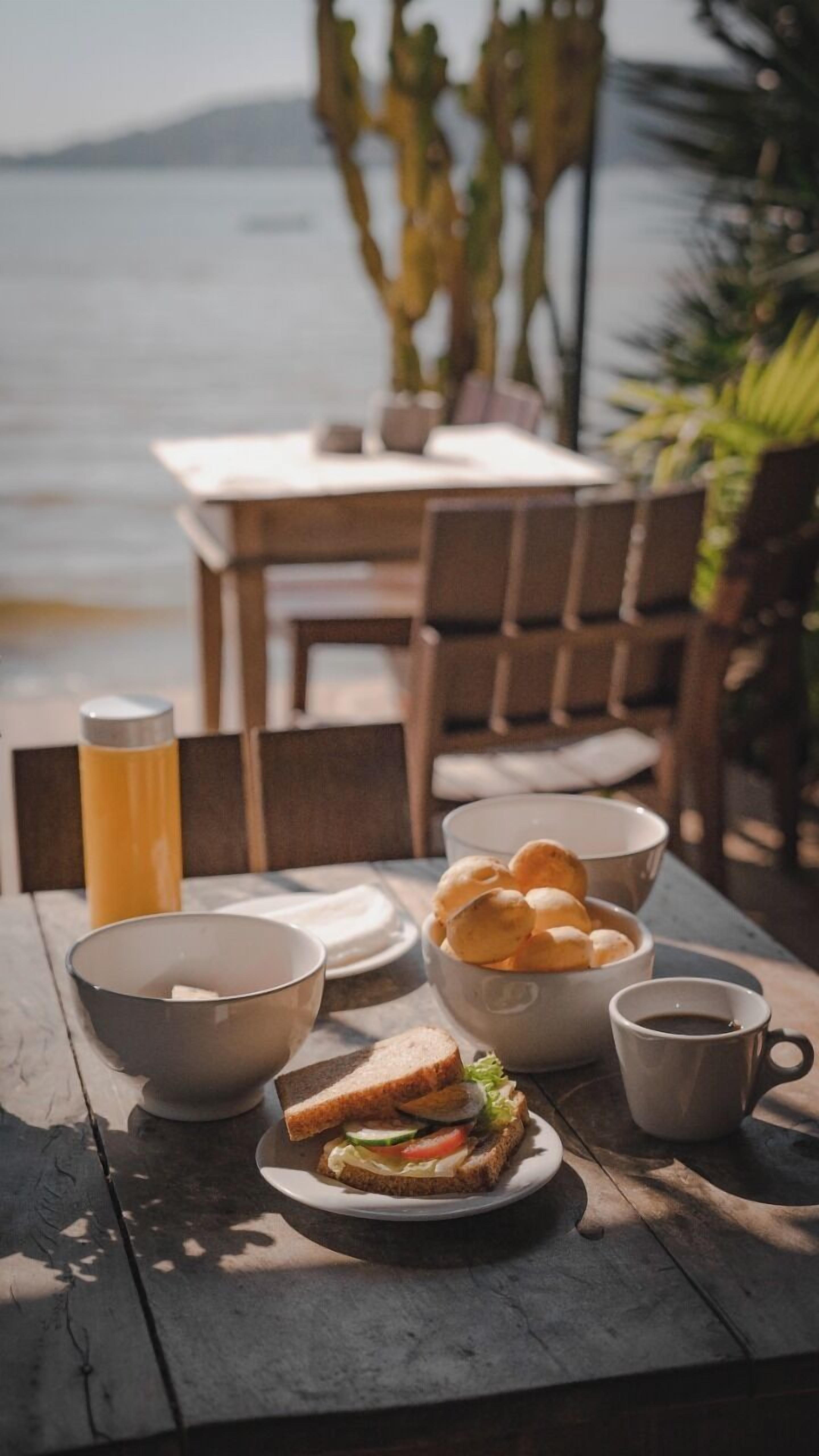 Une table en bois avec un sandwich, un bol, une tasse et une assiette de pain.