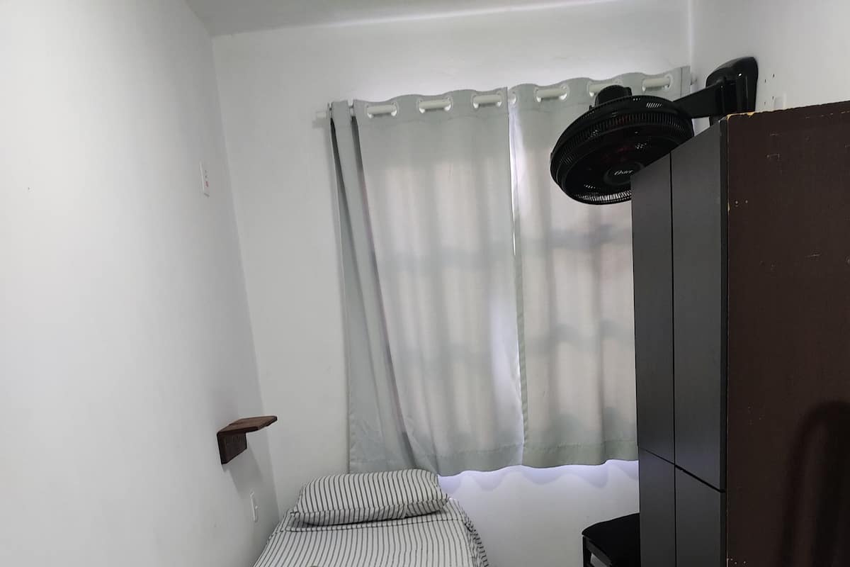 A room with three single beds, a wardrobe, a chair, and a window with curtains.