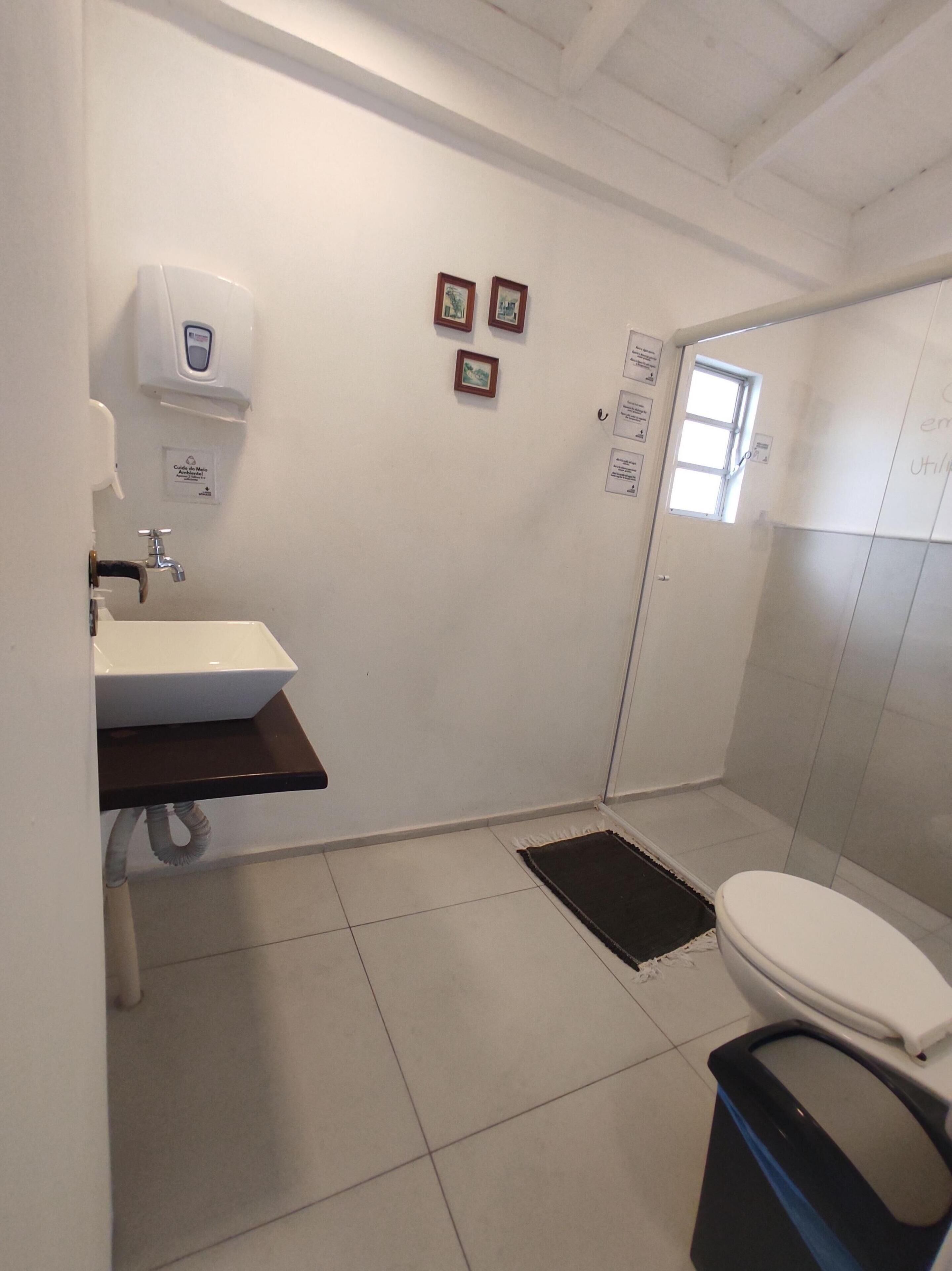 Un baño con lavamanos blanco, inodoro, ducha y una ventana pequeña.
