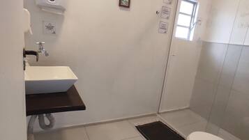 Un baño con lavamanos blanco, inodoro, ducha y una ventana pequeña.