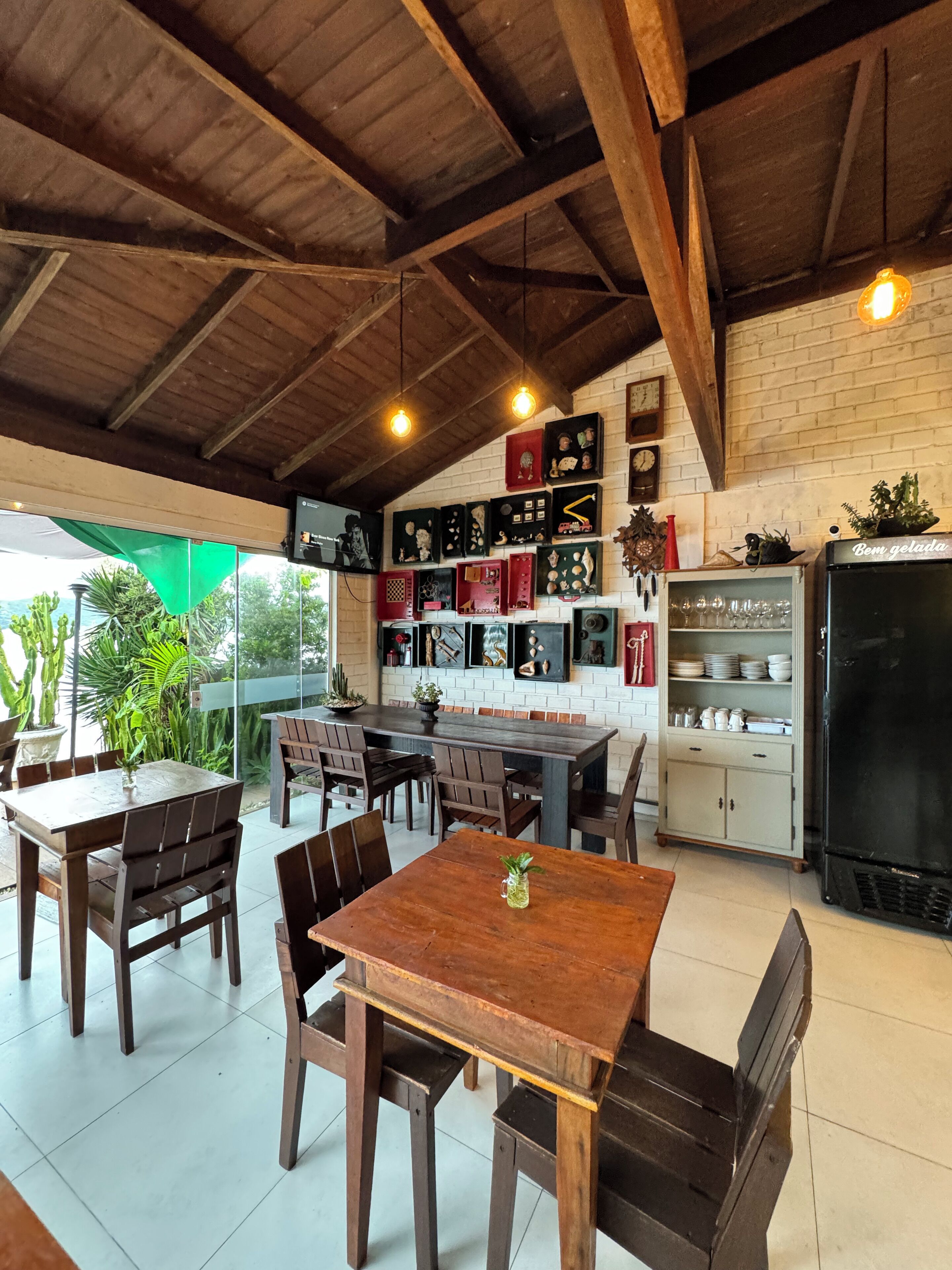 Un coin repas rustique avec des tables et des chaises en bois, un mur de briques orné de tableaux encadrés et un réfrigérateur.