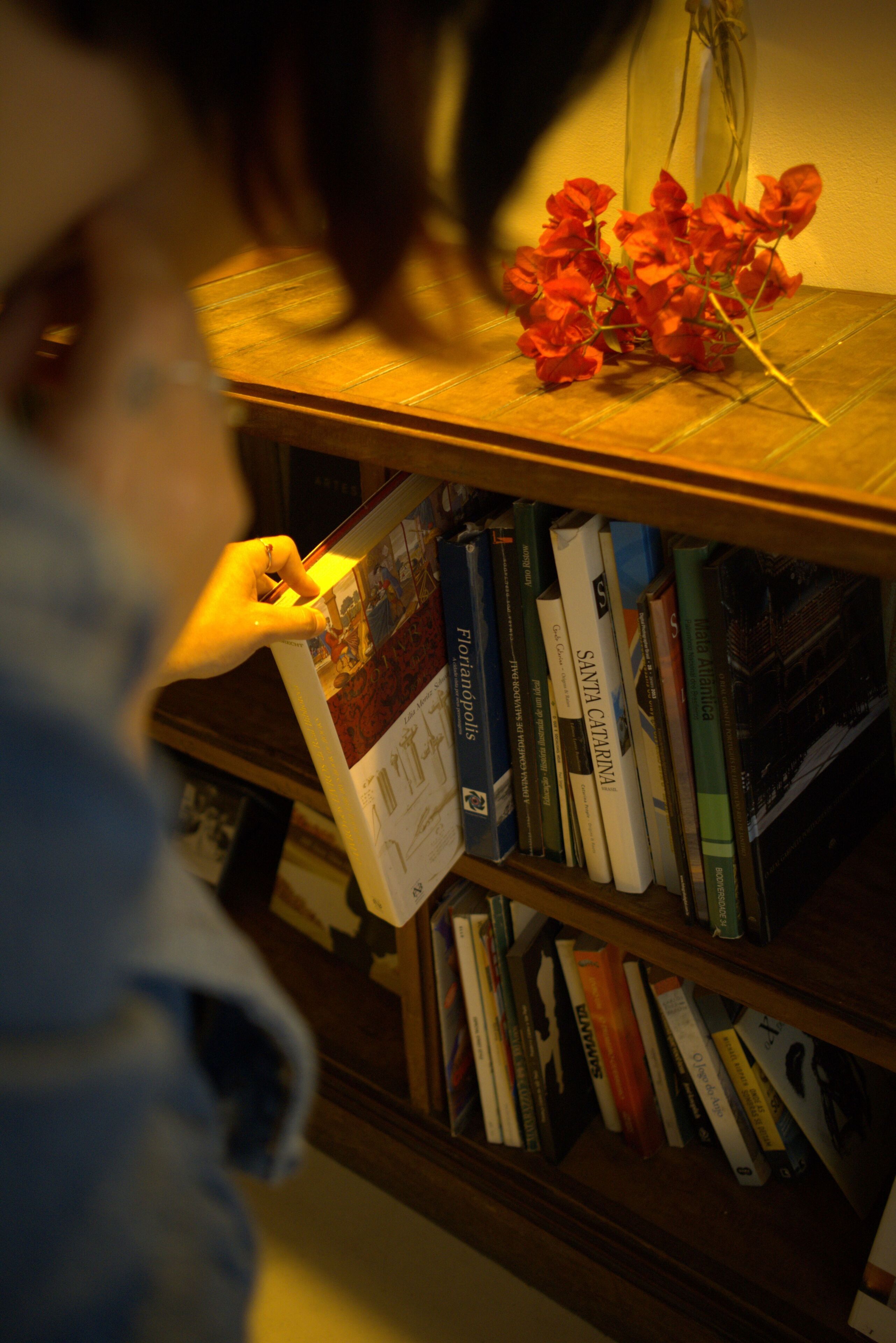A bookshelf with books and a vase with red flowers.