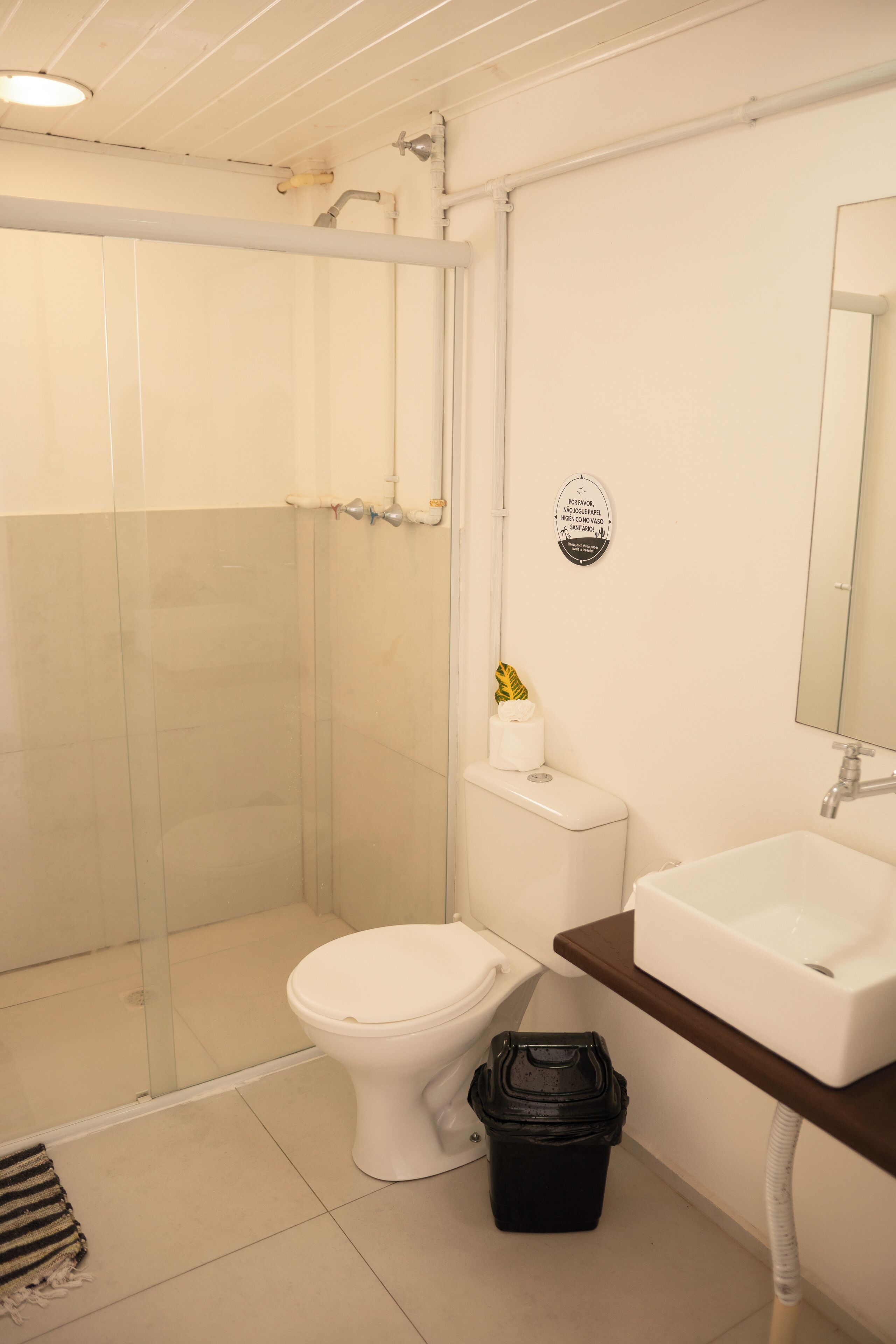 Un baño con cabina de ducha de vidrio, inodoro, lavabo y un cubo de basura.