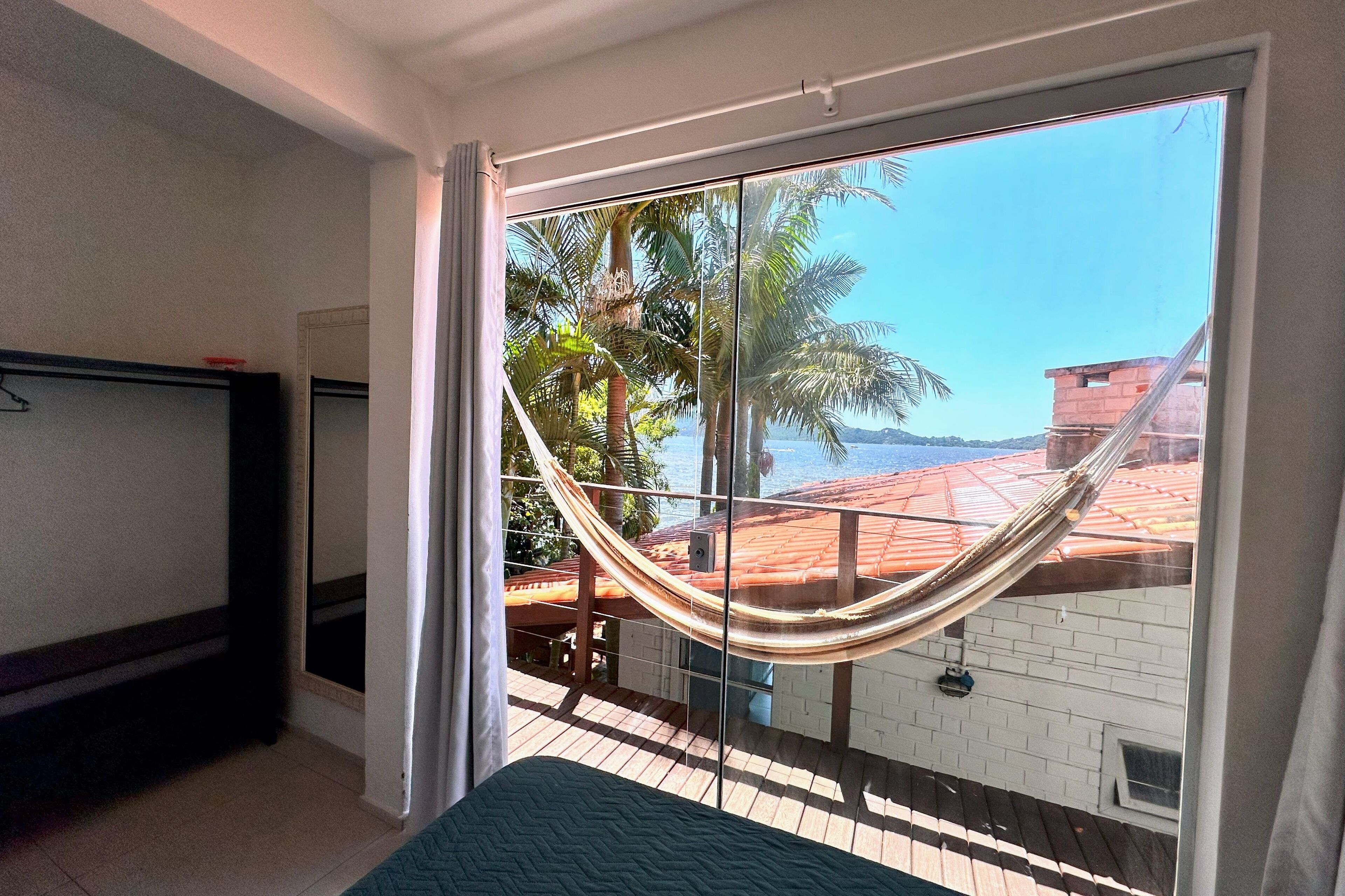 A room with a large window, a hammock, and a view of palm trees and a building.