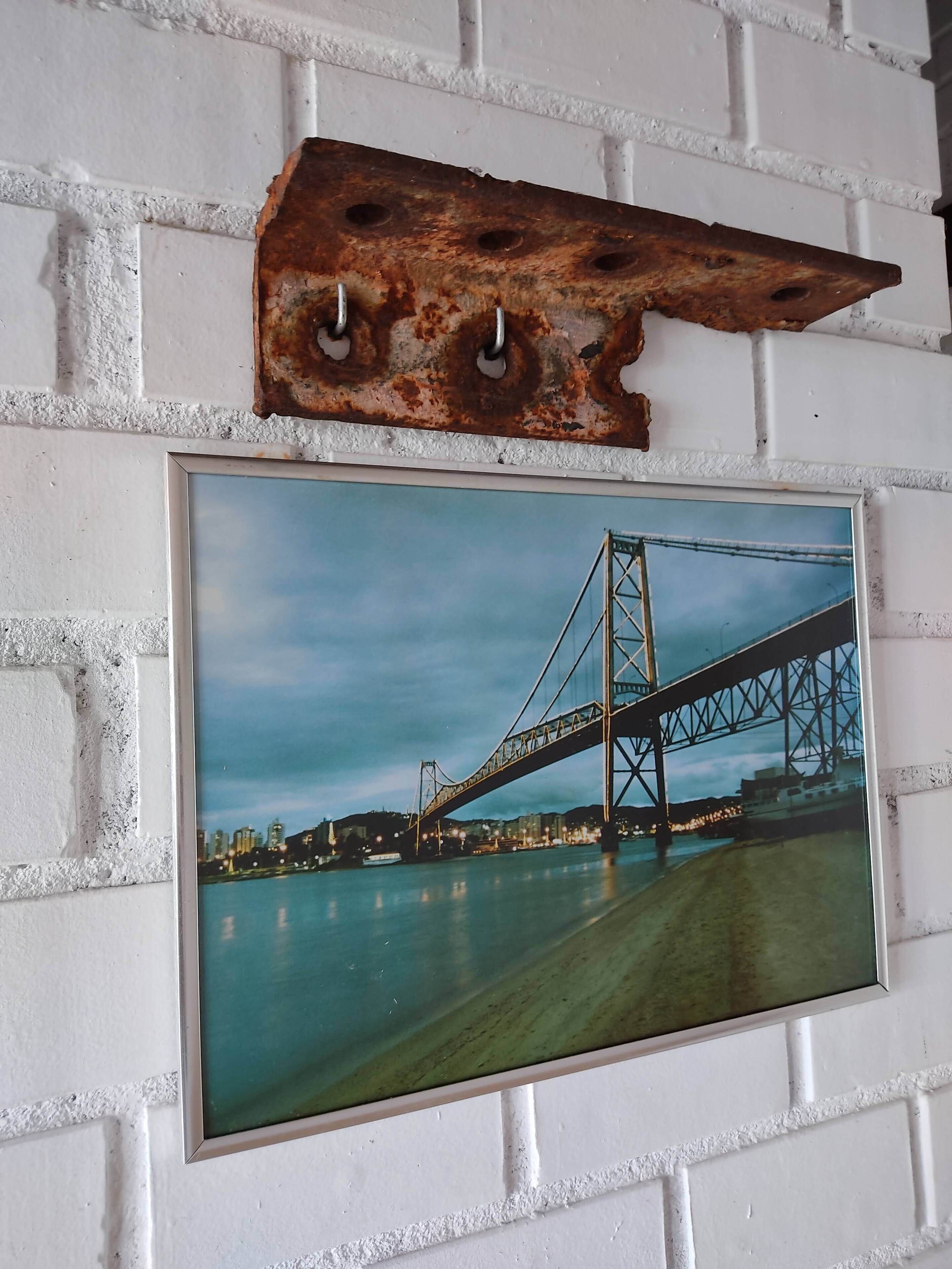 A framed photograph of a bridge on a white brick wall.