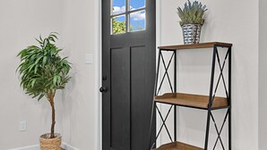 A hallway with a dark door, a potted plant, a metal shelving unit, and a trash bin. - Tiny Twin Lia, New 2 bedroom Fully Furnished Midterm in beautiful Waco (Waco)