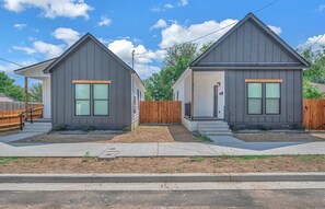 Two single-story houses with grey siding and large windows, each with a front porch and a wooden fence.