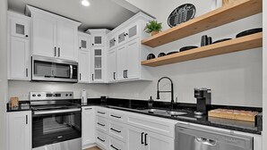 A modern kitchen with white cabinets, stainless steel appliances, a wooden shelf with kitchenware, and a coffee station. - Tiny Twin Lia, New 2 bedroom Fully Furnished Midterm in beautiful Waco (Waco)