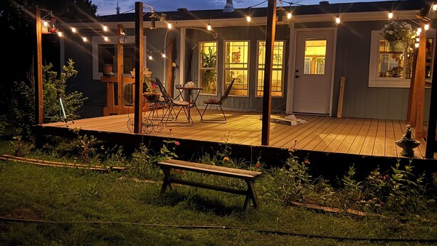 En träveranda med ljusslingor, en bänk och ett hus med fönster och en dörr.