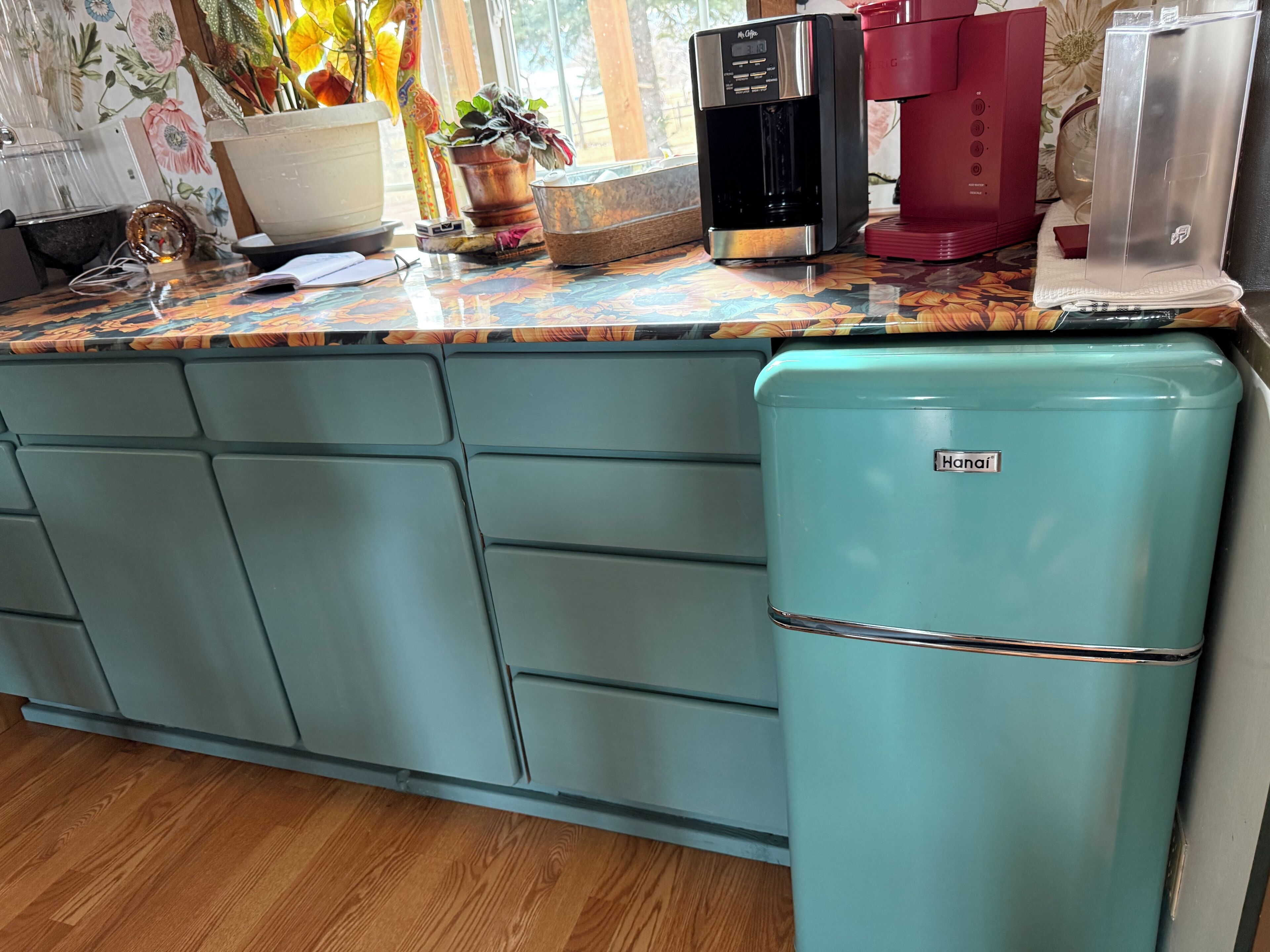 A kitchen with a teal refrigerator, a coffee maker, and a red coffee machine.