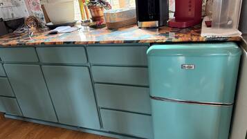 A kitchen with a teal refrigerator, a coffee maker, and a red coffee machine.