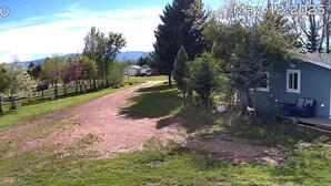 En lantlig fastighet med en grusväg som leder fram till ett hus, omgivet av träd och ett inhägnat område.