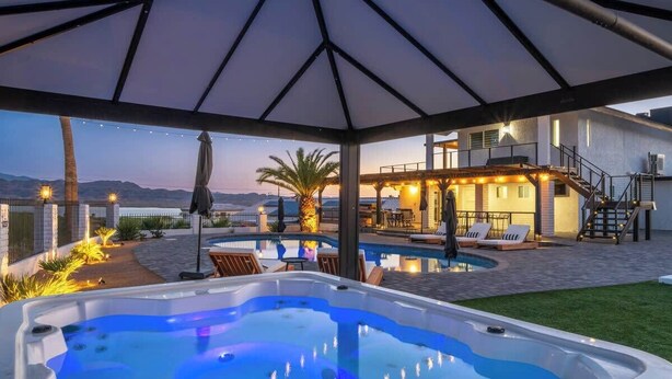 A hot tub under a covered patio with a pool, outdoor furniture, and a staircase leading to a building. - Iconic Views w/Pickleball & Gameroom | Pool & Spa (Lake Havasu City)