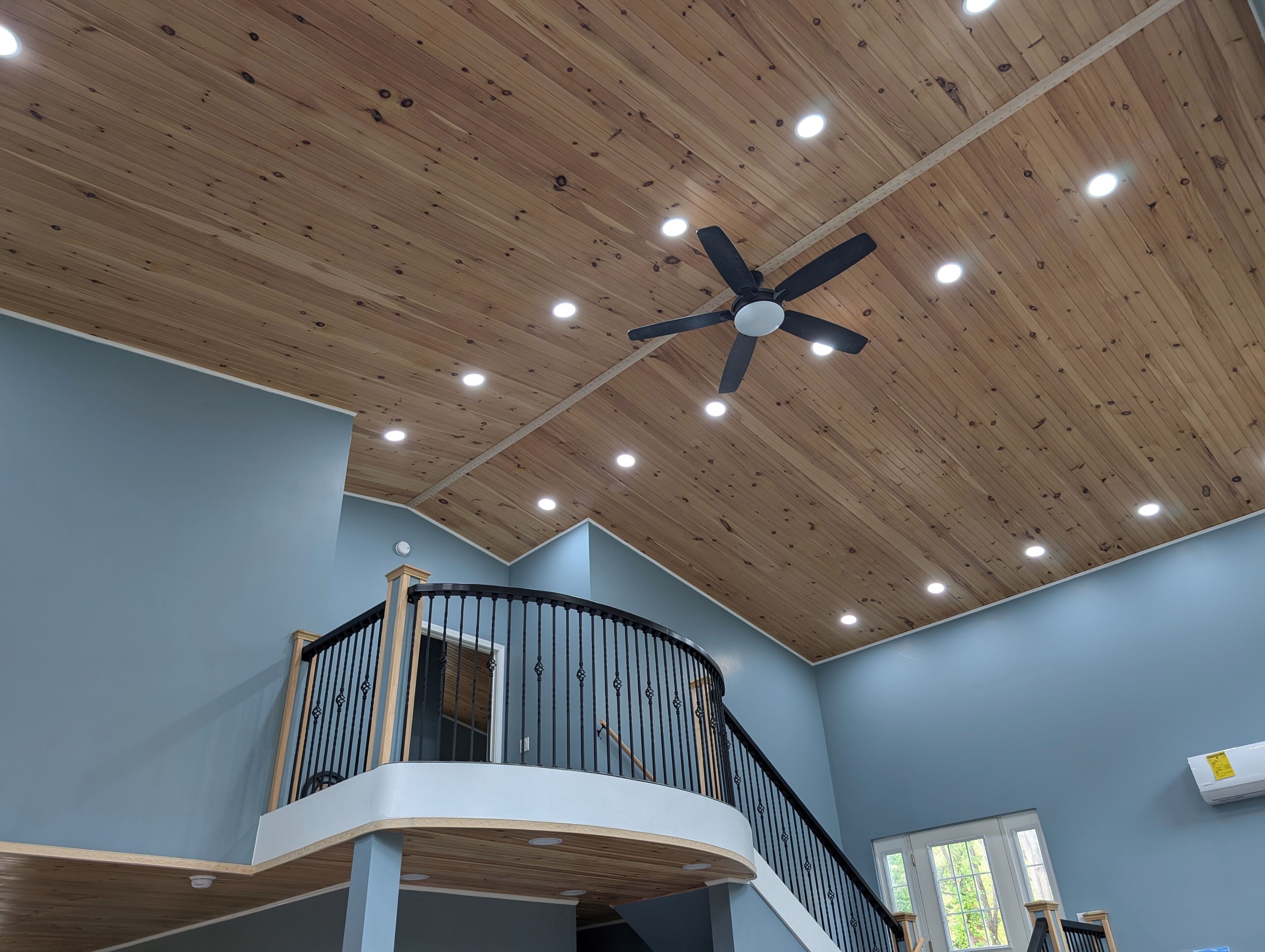 Un intérieur à plusieurs niveaux avec un plafond en bois, un ventilateur de plafond central et une balustrade incurvée.