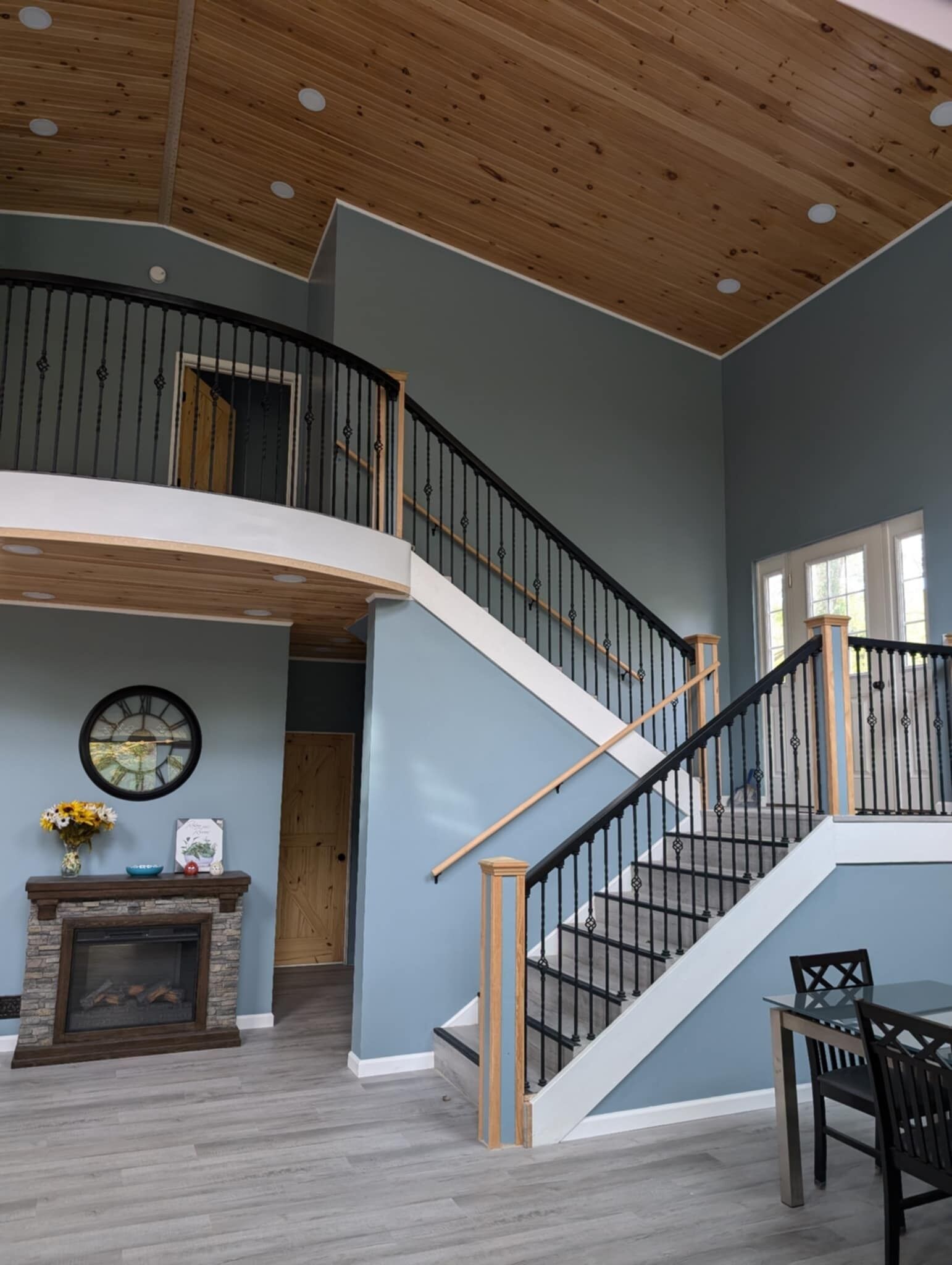 Un intérieur spacieux avec un plafond en bois, un escalier doté de rampes noires et une cheminée avec un manteau en pierre.