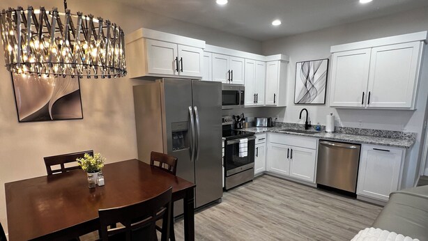 Una cocina moderna con armarios blancos, electrodomésticos de acero inoxidable y un comedor con mesa y sillas de madera.